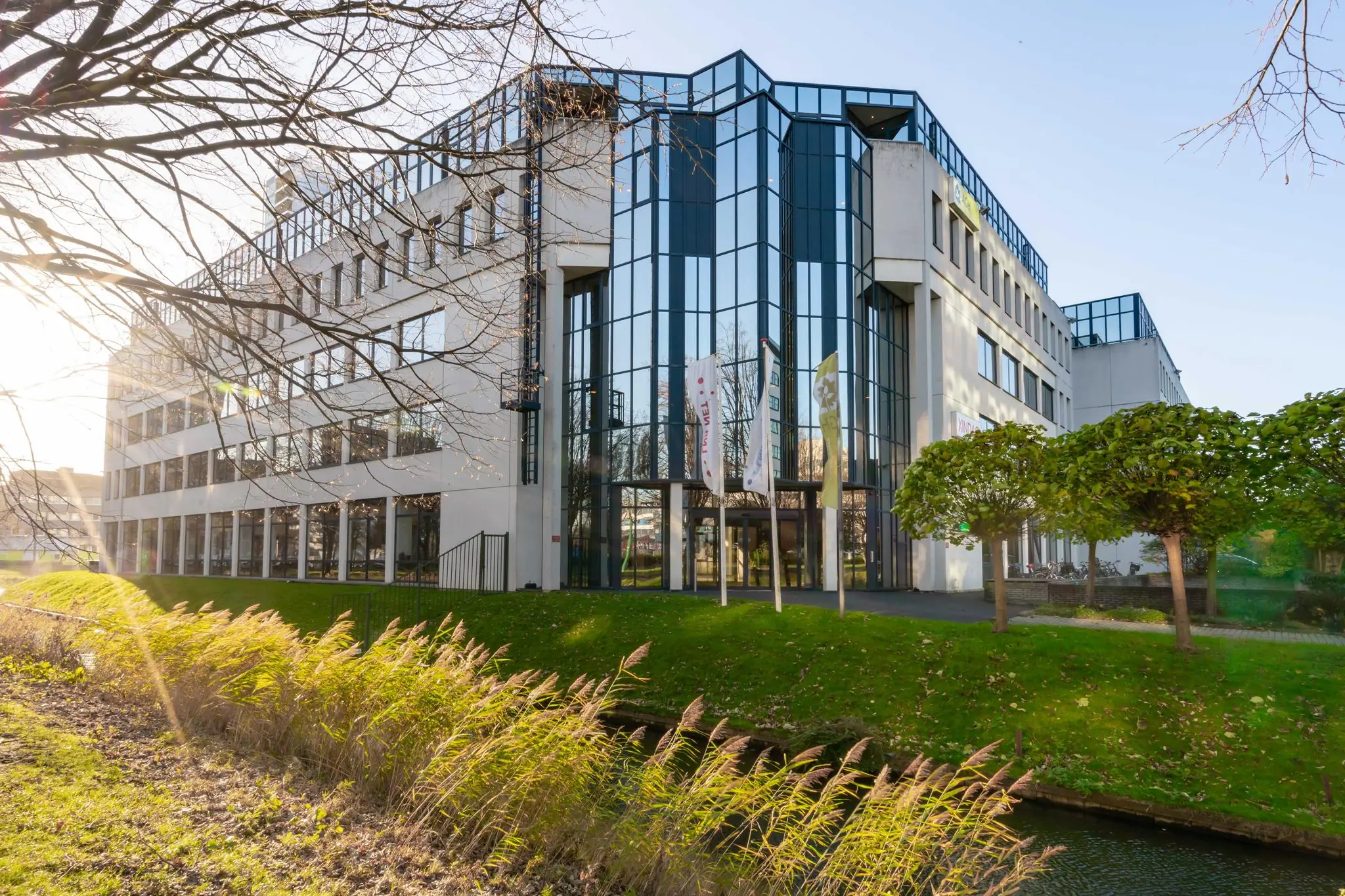 Modern kantoorgebouw aan de De Bruyn Kopsstraat met grote ramen en vlaggen bij de entree.